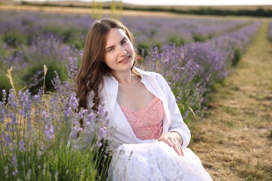 Photo of Beautiful young woman sitting among lavender flowers outdoors