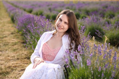 Photo of Beautiful young woman sitting among lavender flowers outdoors
