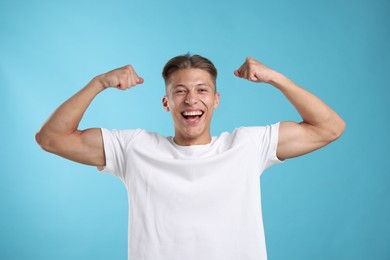 Photo of Strength. Happy man showing his biceps on light blue background