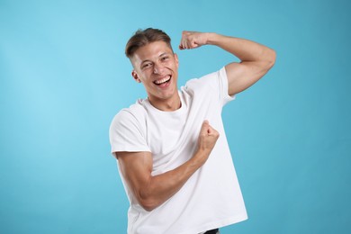 Photo of Strength. Happy man showing his biceps on light blue background