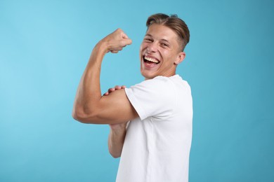 Photo of Strength. Happy man showing his biceps on light blue background