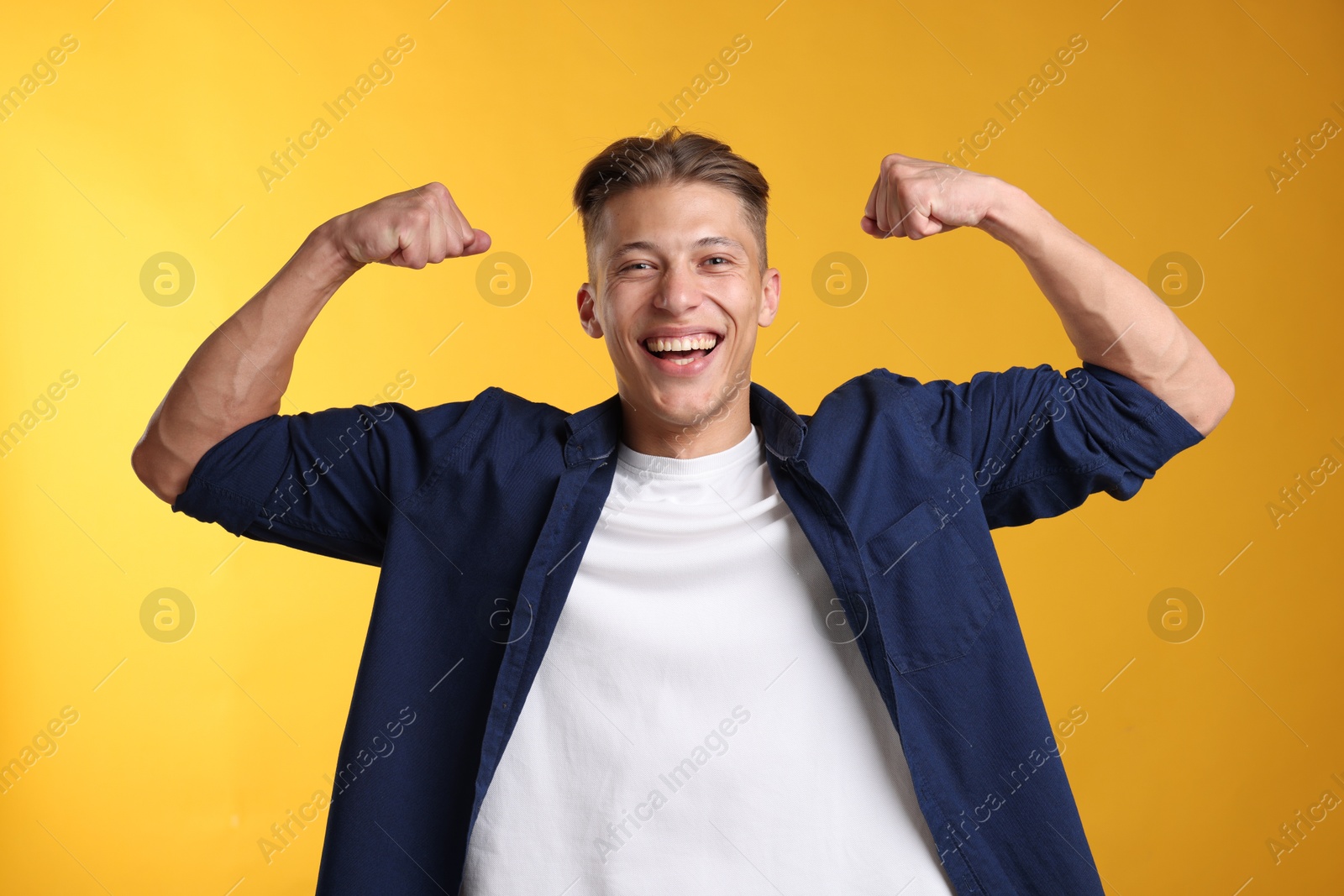 Photo of Strength. Happy man showing his biceps on yellow background