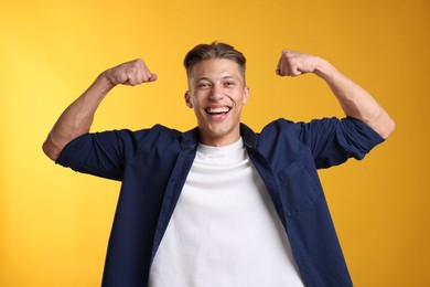 Photo of Strength. Happy man showing his biceps on yellow background
