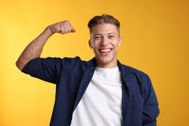 Photo of Strength. Happy man showing his biceps on yellow background