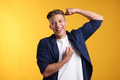 Photo of Strength. Happy man showing his biceps on yellow background