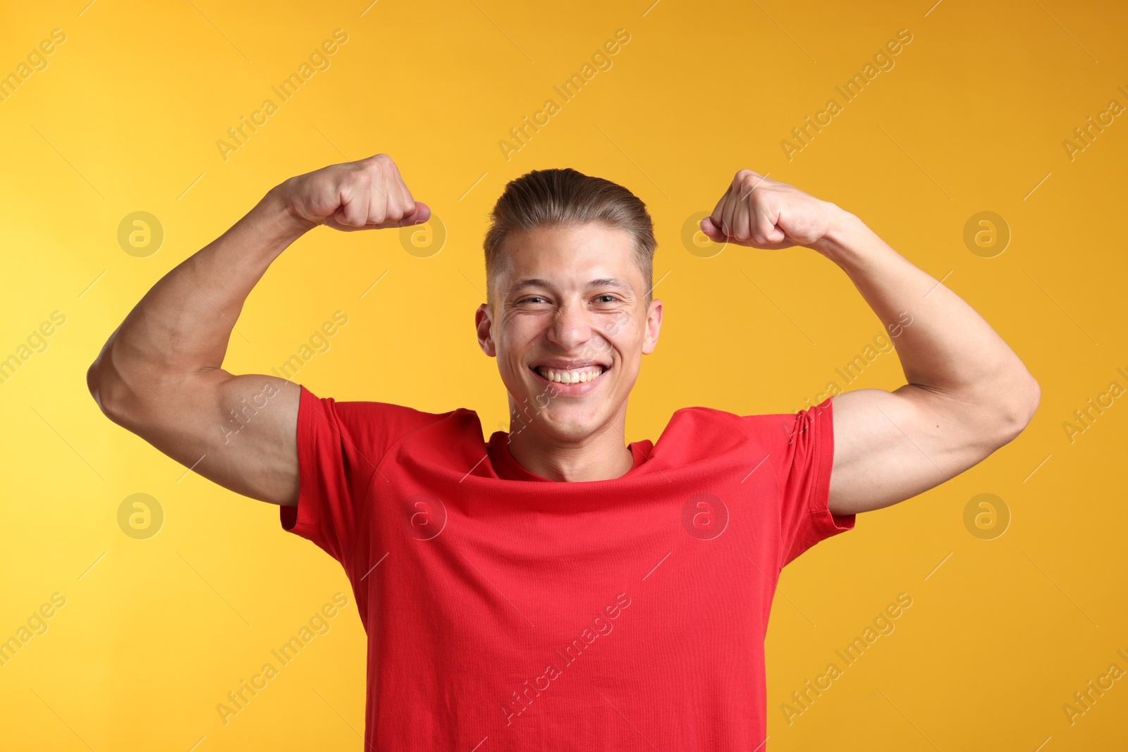 Strength. Happy man showing his biceps on yellow background Photo of Strength. Happy man showing his biceps on yellow background