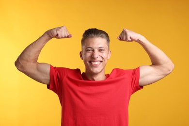 Photo of Strength. Happy man showing his biceps on yellow background