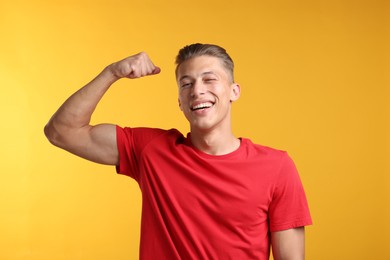 Photo of Strength. Happy man showing his biceps on yellow background