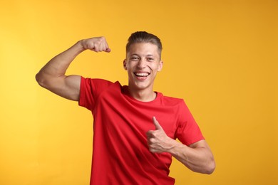 Photo of Strength. Happy man showing his biceps and thumbs up on yellow background