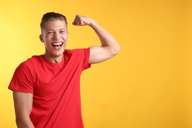 Photo of Strength. Happy man showing his biceps on yellow background. Space for text