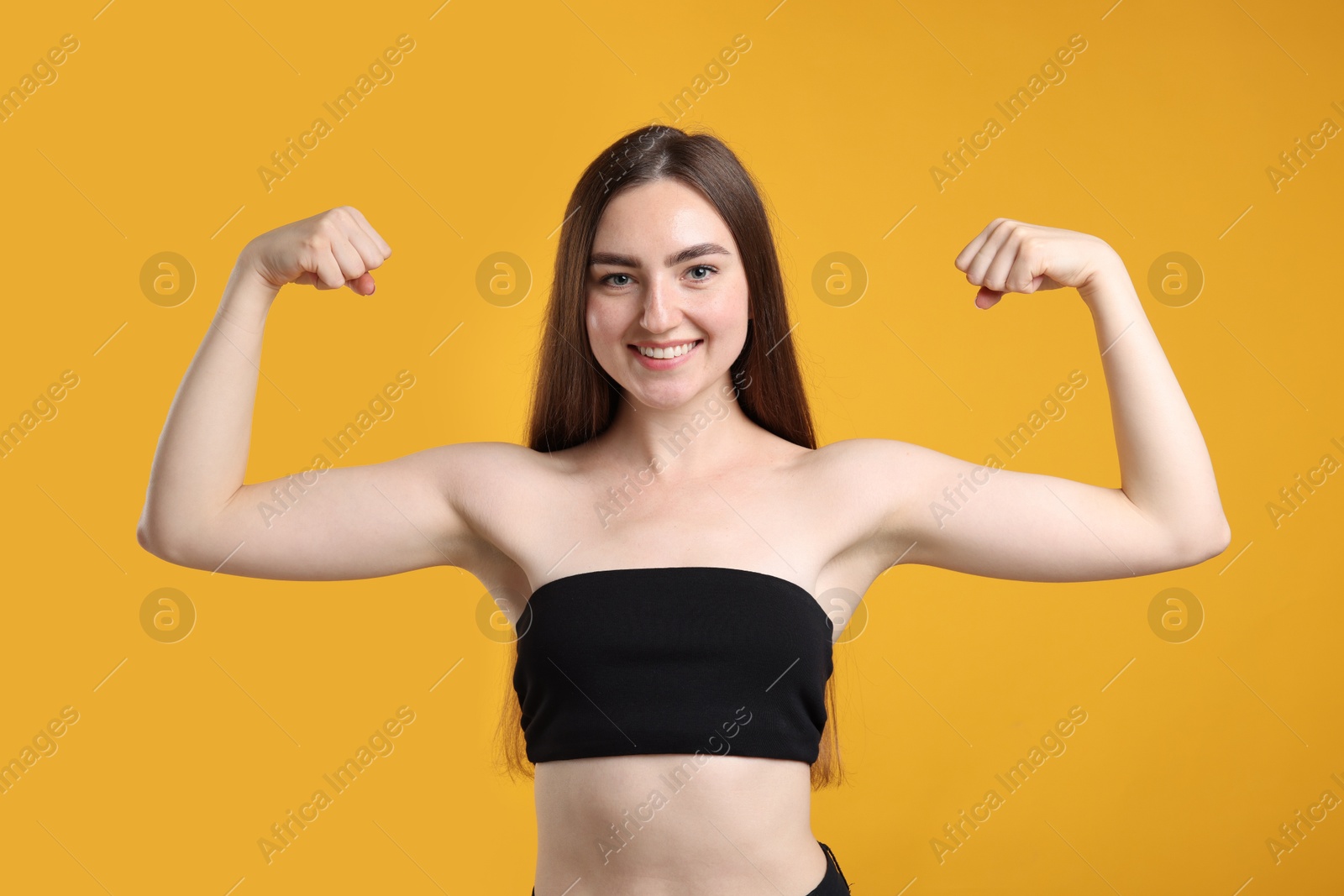 Strength. Happy woman showing her biceps on yellow background Photo of Strength. Happy woman showing her biceps on yellow background