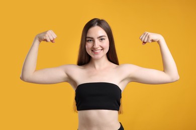 Photo of Strength. Happy woman showing her biceps on yellow background