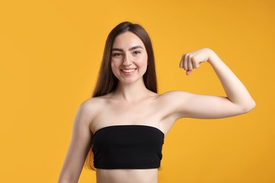 Photo of Strength. Happy woman showing her biceps on yellow background