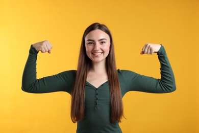 Photo of Strength. Happy woman showing her biceps on yellow background