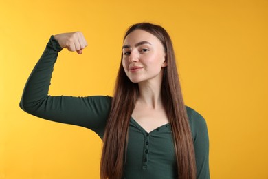 Photo of Strength. Proud woman showing her biceps on yellow background