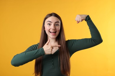 Photo of Strength. Happy woman pointing at her biceps on yellow background