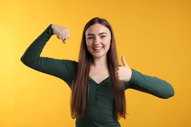 Photo of Strength. Happy woman showing her biceps and thumbs up on yellow background