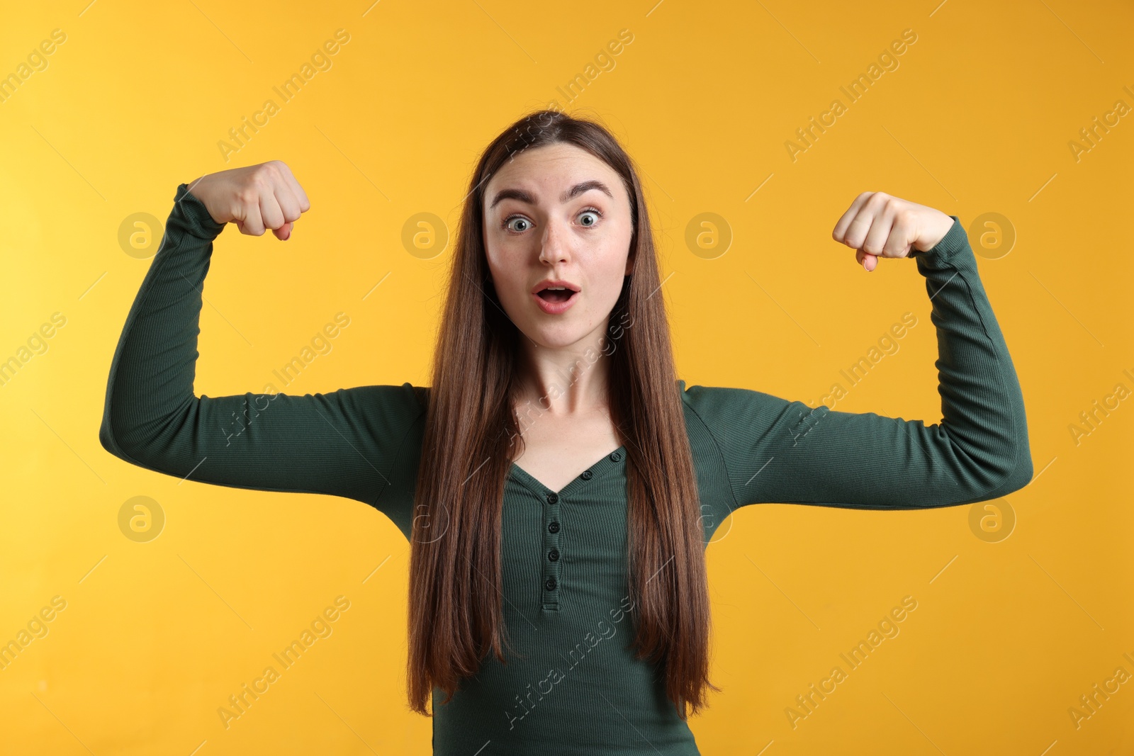 Photo of Strength. Surprised woman showing her biceps on yellow background