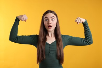 Photo of Strength. Surprised woman showing her biceps on yellow background