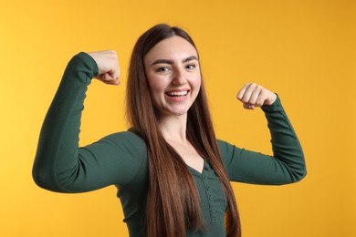 Photo of Strength. Happy woman showing her biceps on yellow background
