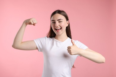 Photo of Strength. Happy woman showing her biceps and thumbs up on pink background