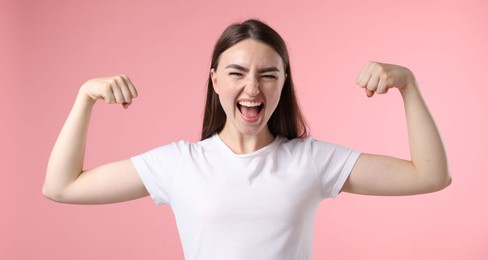 Photo of Strength. Emotional woman showing her biceps on pink background