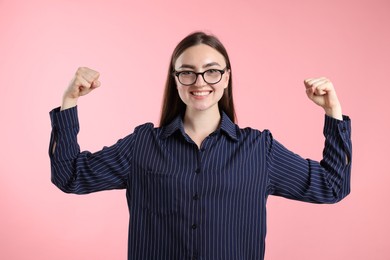 Photo of Strength. Happy businesswoman in glasses showing her biceps on pink background