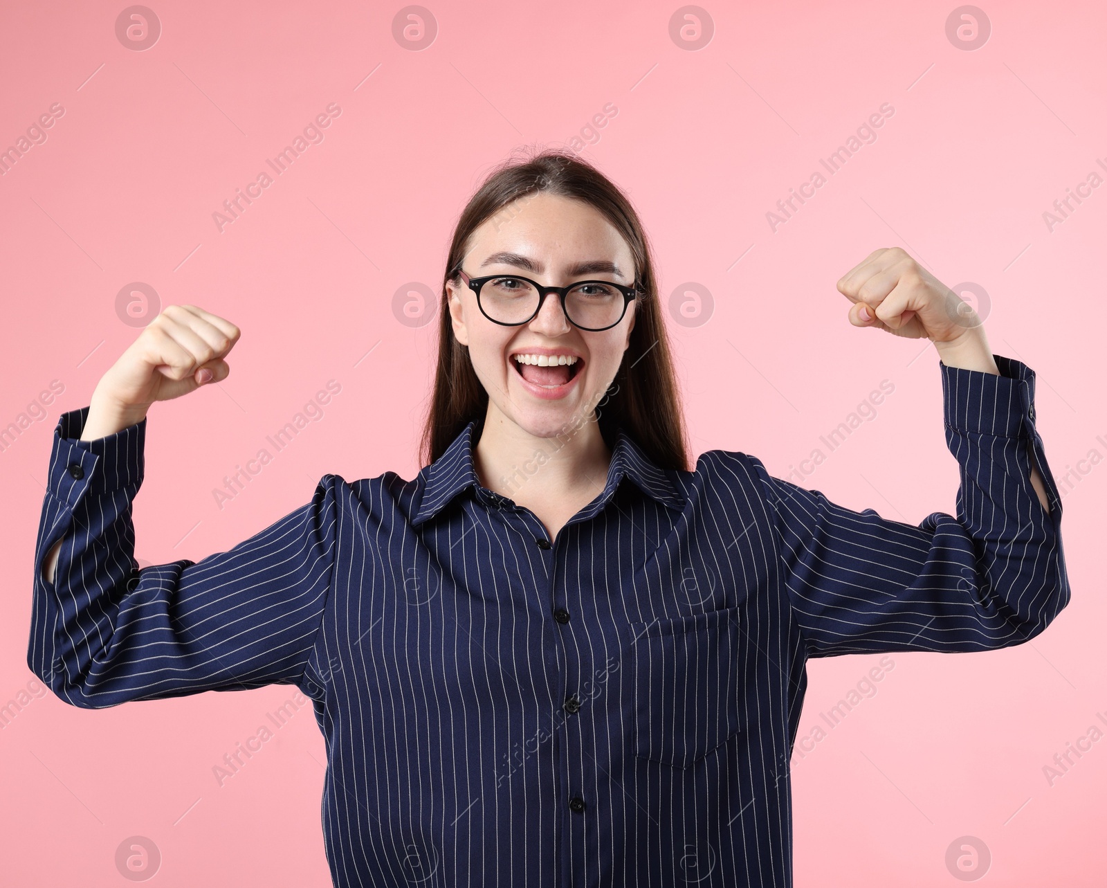 Photo of Strength. Happy businesswoman in glasses showing her biceps on pink background