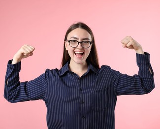Photo of Strength. Happy businesswoman in glasses showing her biceps on pink background