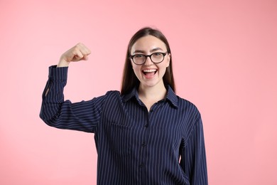 Photo of Strength. Happy businesswoman in glasses showing her biceps on pink background