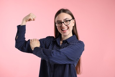 Photo of Strength. Happy businesswoman in glasses showing her biceps on pink background
