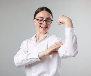 Photo of Strength. Happy businesswoman in glasses showing her biceps on grey background
