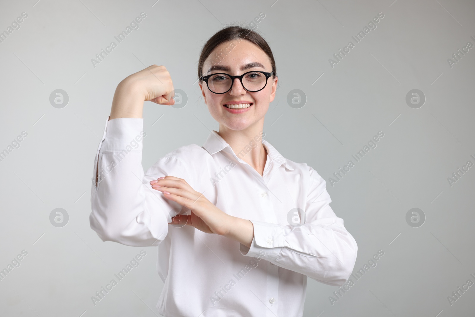 Photo of Strength. Happy businesswoman in glasses showing her biceps on grey background