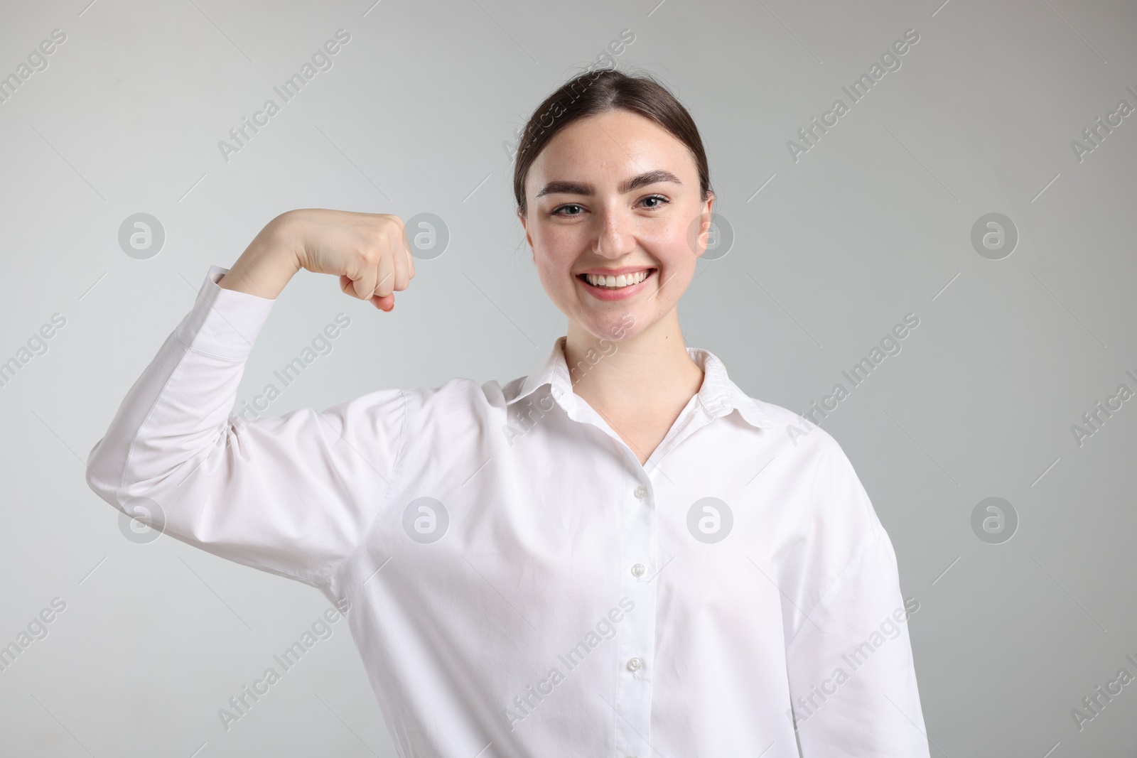 Strength. Happy businesswoman showing her biceps on grey background Photo of Strength. Happy businesswoman showing her biceps on grey background