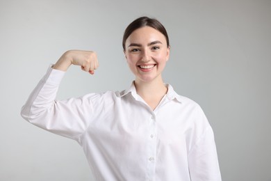 Photo of Strength. Happy businesswoman showing her biceps on grey background