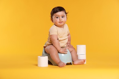 Photo of Cute little baby sitting on potty and rolls of toilet paper against orange background