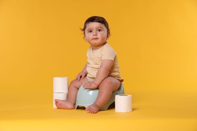 Photo of Cute little baby sitting on potty and rolls of toilet paper against orange background