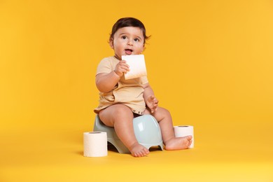 Photo of Cute little baby sitting on potty and rolls of toilet paper against orange background