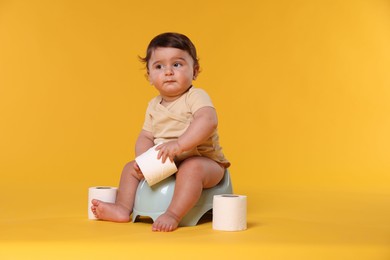 Photo of Cute little baby sitting on potty and rolls of toilet paper against orange background