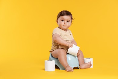 Photo of Cute little baby sitting on potty and rolls of toilet paper against orange background