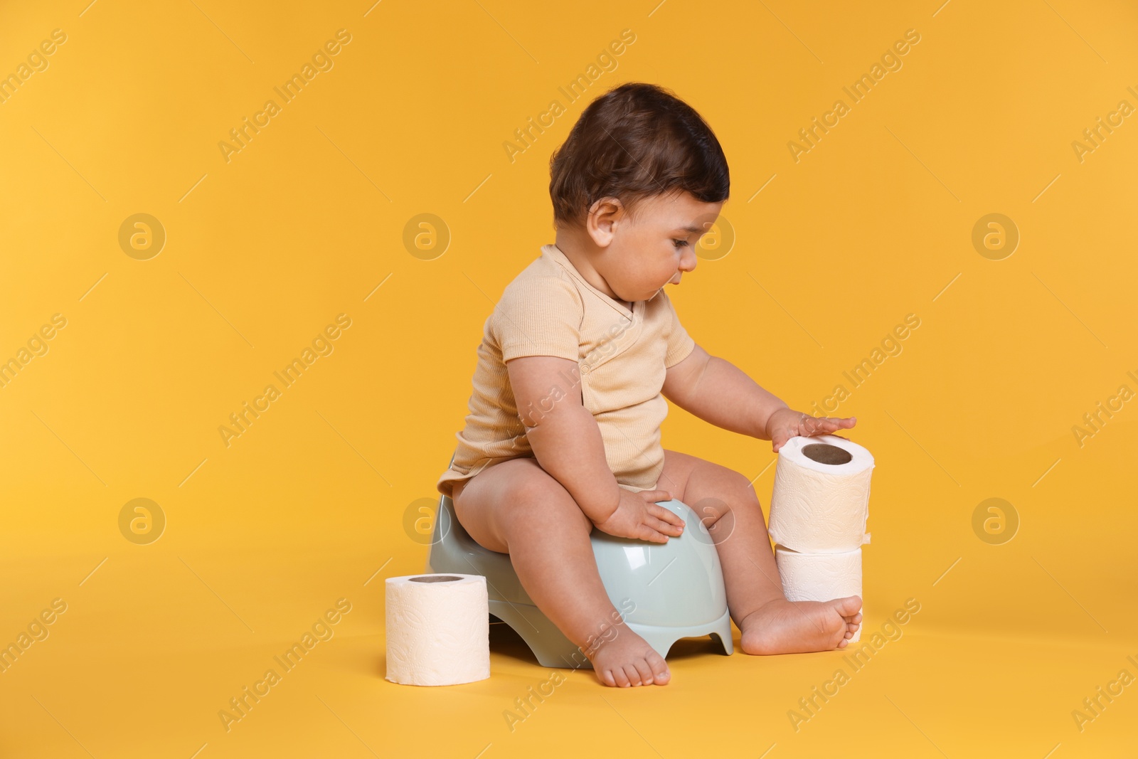 Cute little baby sitting on potty and rolls of toilet paper against orange background Photo of Cute little baby sitting on potty and rolls of toilet paper against orange background