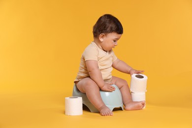 Photo of Cute little baby sitting on potty and rolls of toilet paper against orange background