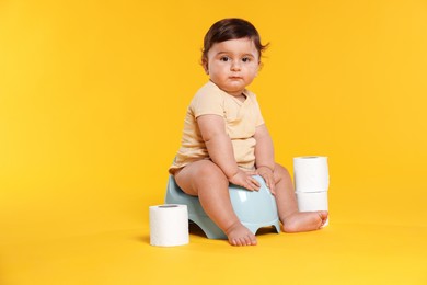 Photo of Cute little baby sitting on potty and rolls of toilet paper against orange background