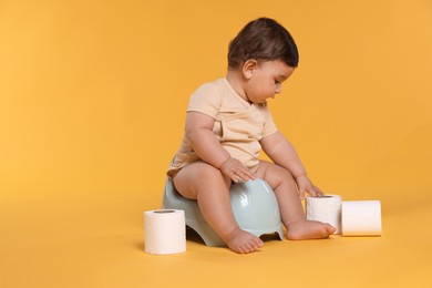 Photo of Cute little baby sitting on potty and rolls of toilet paper against orange background