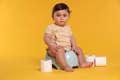 Photo of Cute little baby sitting on potty and rolls of toilet paper against orange background