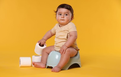 Photo of Cute little baby sitting on potty and rolls of toilet paper against orange background