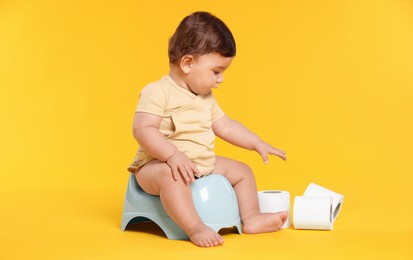 Photo of Cute little baby sitting on potty and rolls of toilet paper against orange background