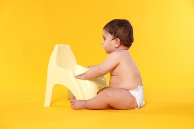 Photo of Cute little baby sitting near potty on orange background