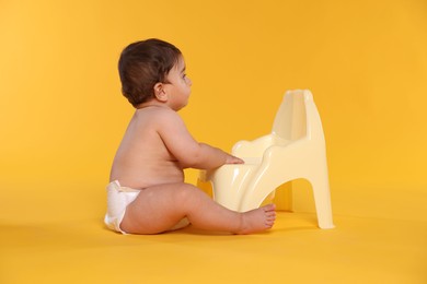 Photo of Cute little baby sitting near potty on orange background