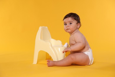 Photo of Cute little baby sitting near potty on orange background